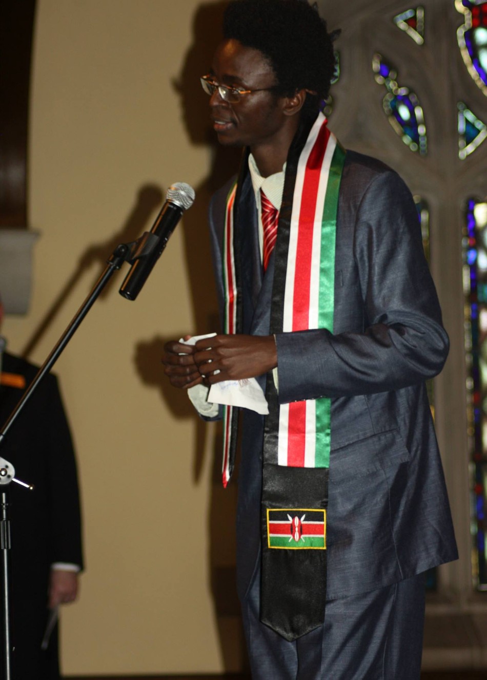 Janek Sunga speaking at a public event, wearing a Kenyan flag sash
